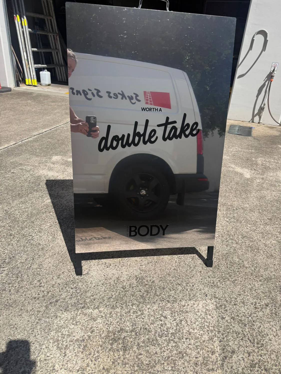 Mirror A-frame sign standing outside reflecting a work van