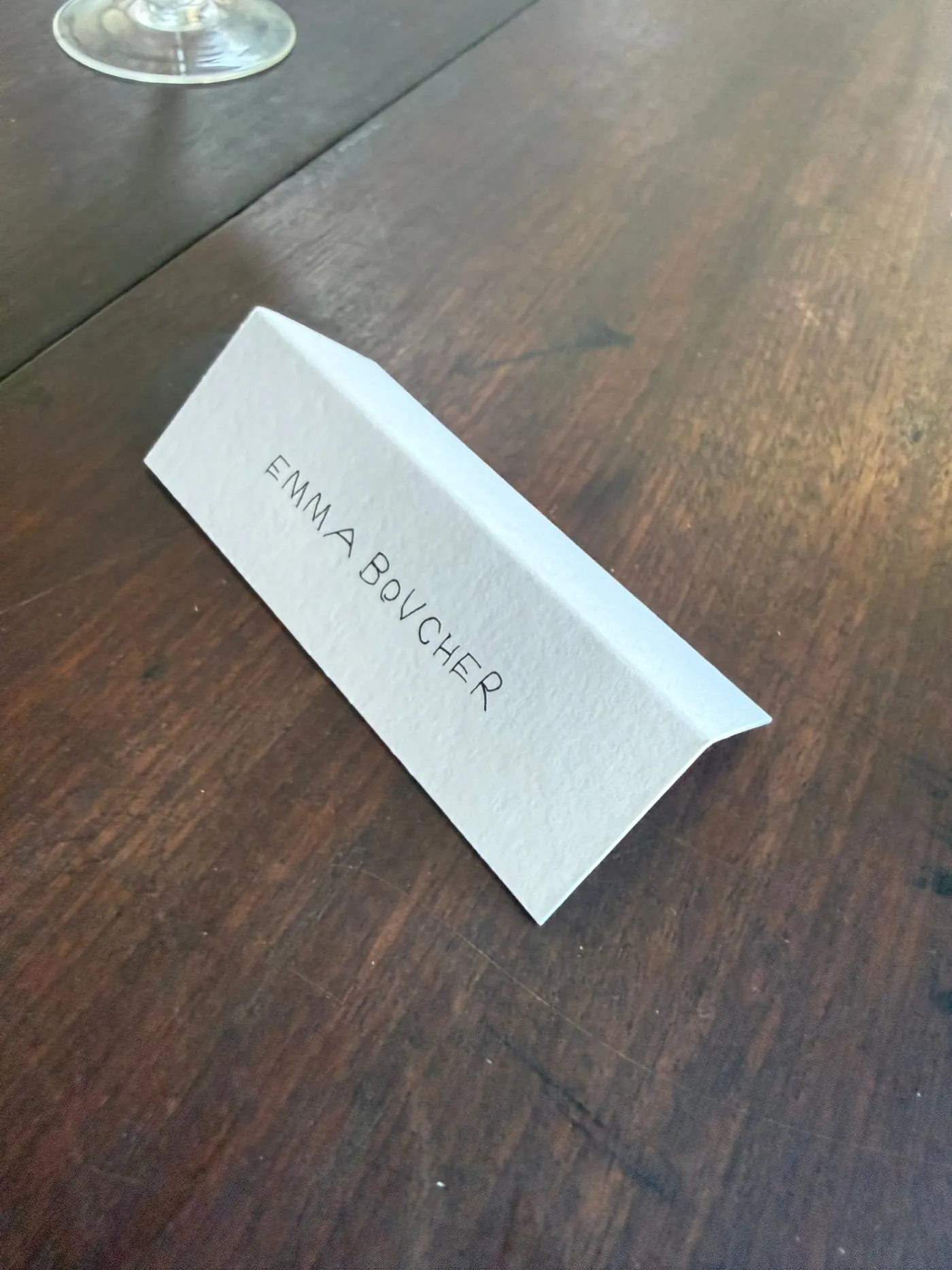 Folded place card standing on a timber table with a guest name in handwritten lettering