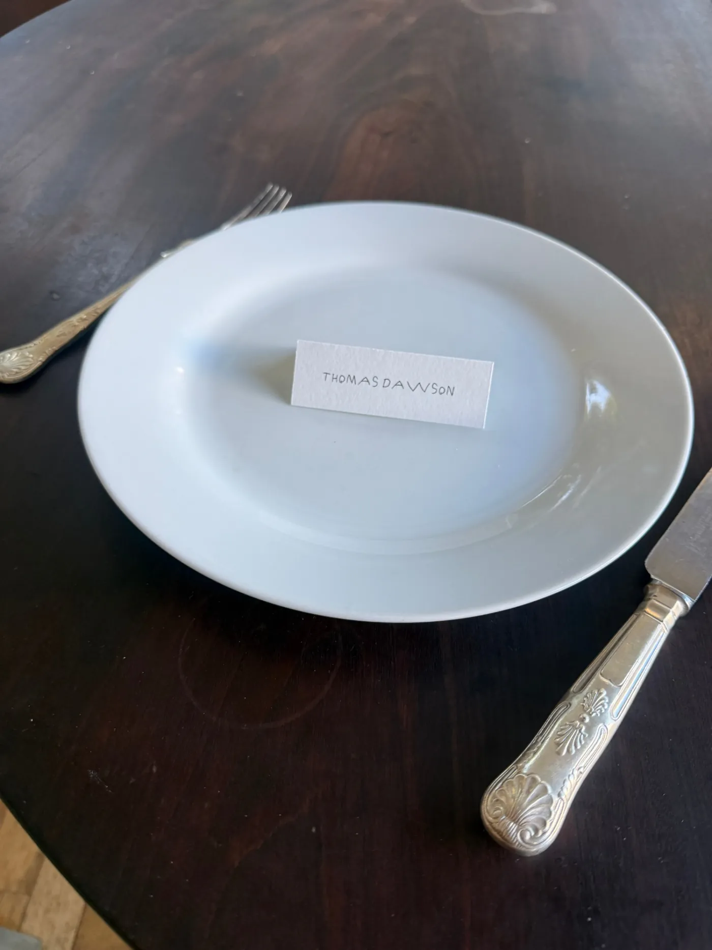 Flat place card with a guest name in handwritten lettering on a dinner plate