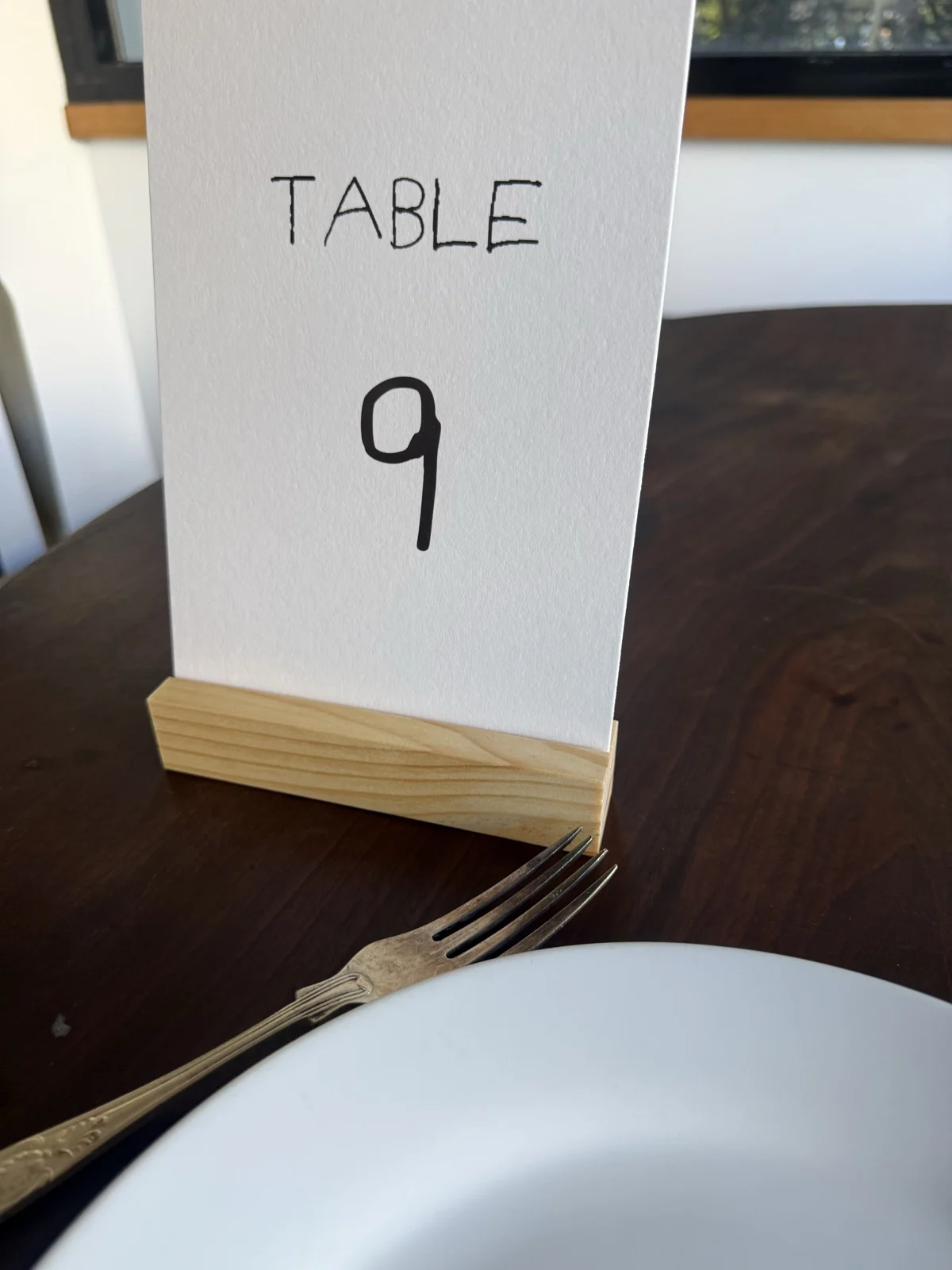 Table 9 number card in handwritten lettering standing in a pale timber stand on a dark wooden table