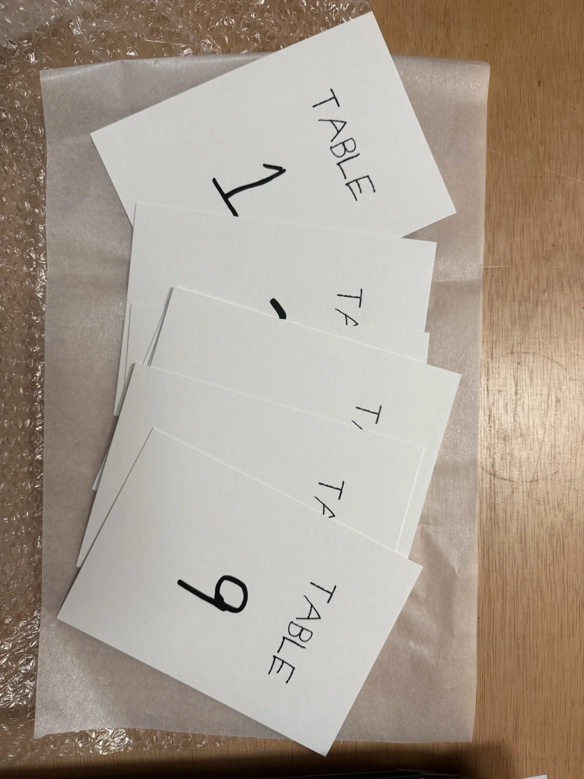 A fan of white table number cards, numbered one to nine, printed in handwritten lettering